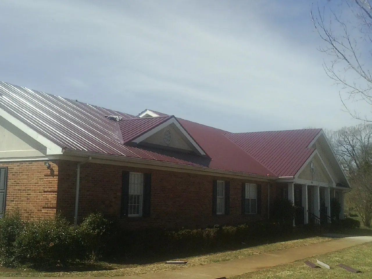 Red metal roof with gabled entries on a long brick building, from a Hail Damage Roof Repair job in Baxter