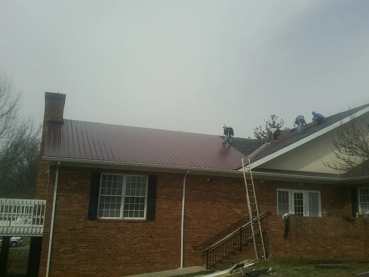 Crew setting red metal roofing panels on a brick home in Baxter