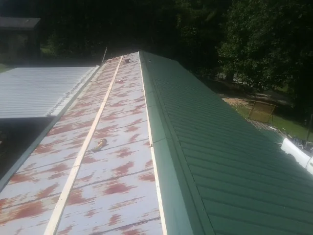 Old rusted panels beside newly installed green metal roofing — Wind Damage Roof Repair by Roofing Brothers in Baxter
